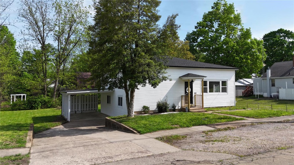 View of front facade featuring concrete driveway, fence, a front yard, and an attached carport