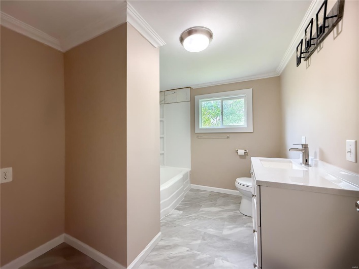 Full bath featuring crown molding, vanity, toilet, baseboards, and a tub to relax in