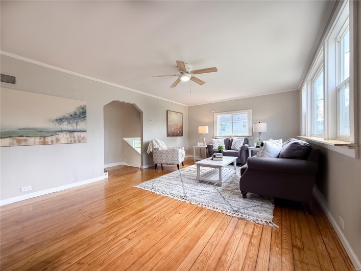 Living room with arched walkways, ceiling fan, wood-type flooring, and baseboards