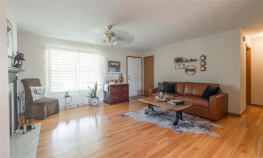 Living area featuring light wood-style floors, ceiling fan, and a fireplace with raised hearth