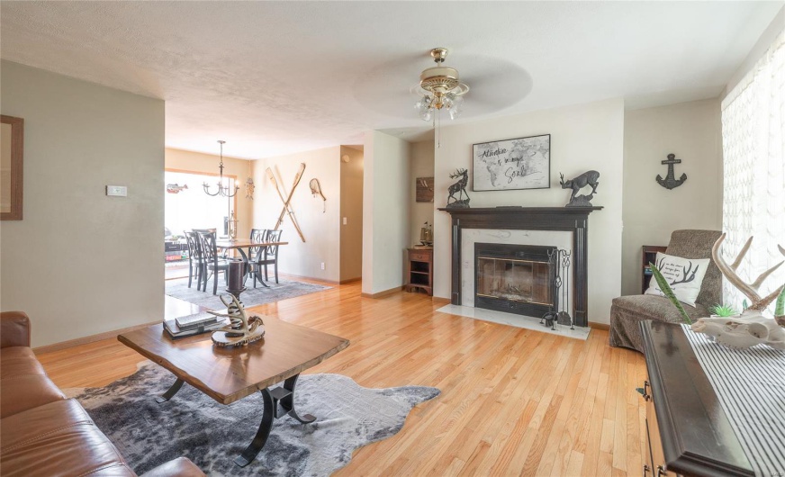 Living area with light wood-type flooring, baseboards, a fireplace with flush hearth, and ceiling fan with notable chandelier