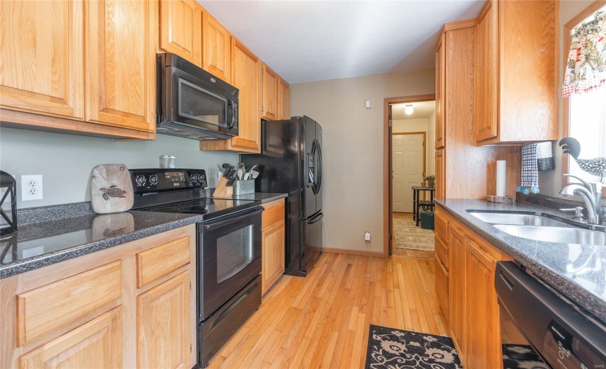 Kitchen featuring dark stone counters, a sink, light wood-type flooring, black appliances, and baseboards
