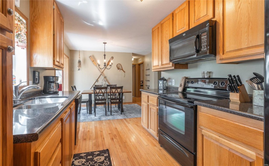 Kitchen with an inviting chandelier, light wood-style floors, brown cabinets, black appliances, and a sink