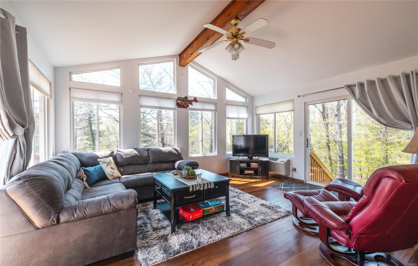 Living area featuring wood finished floors, ceiling fan, and vaulted ceiling with beams