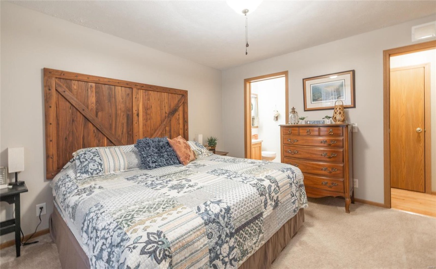 Bedroom with baseboards, visible vents, connected bathroom, and light colored carpet