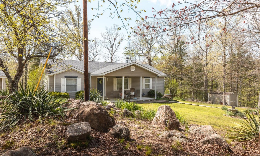 View of front of property featuring a porch, a storage unit, a shingled roof, an outbuilding, and a front yard