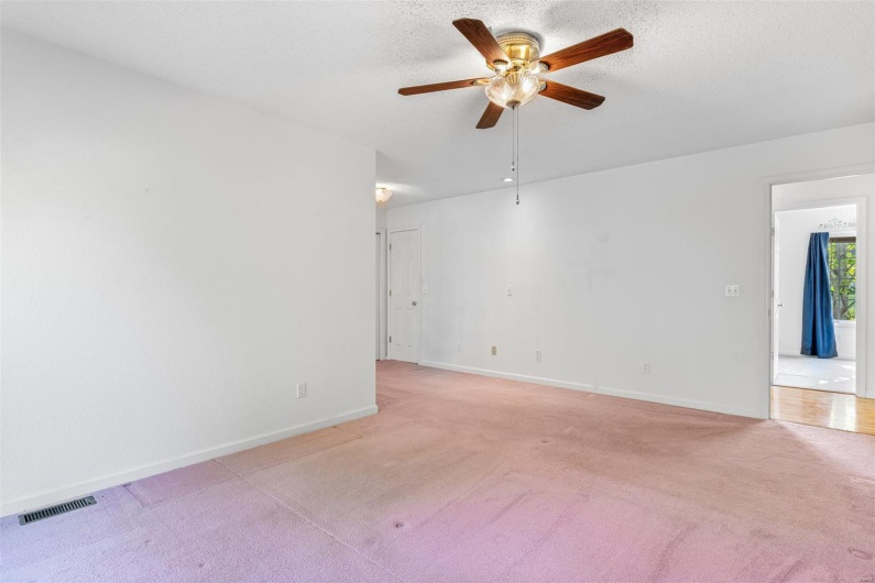 Primary bedroom with ceiling fan, visible vents, light carpet, and baseboards