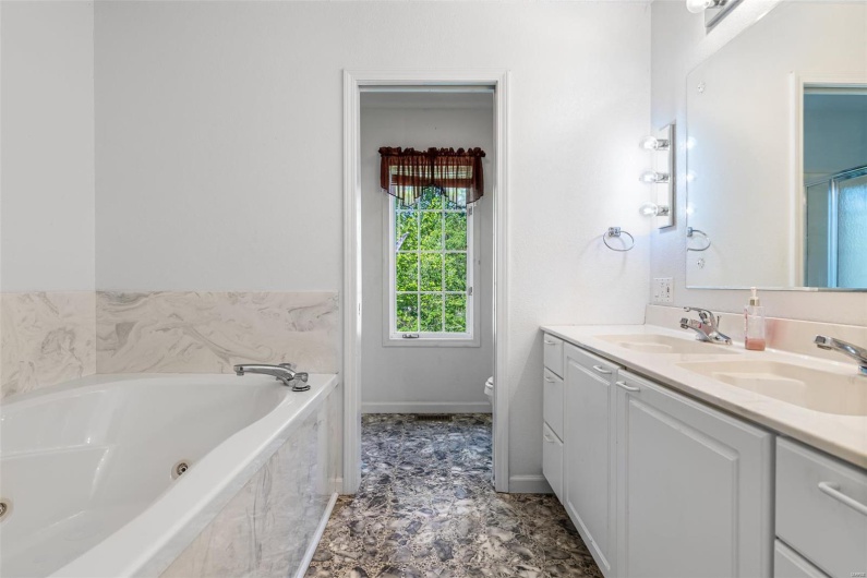 Primary Bathroom featuring double vanity, toilet, a tub with jets, and a sink
