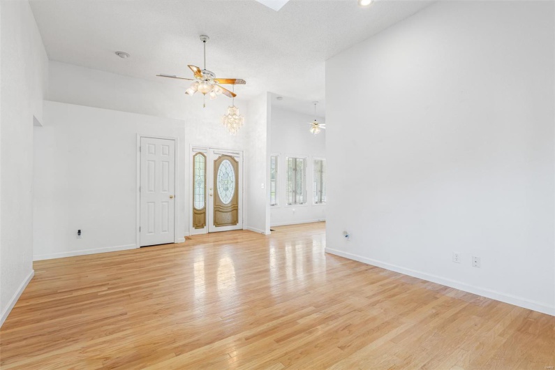 Unfurnished living room with light wood flooring, a ceiling fan, baseboards, and a towering ceiling