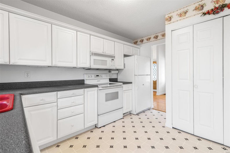 Kitchen featuring dark countertops, white cabinets, white appliances, and a textured ceiling
