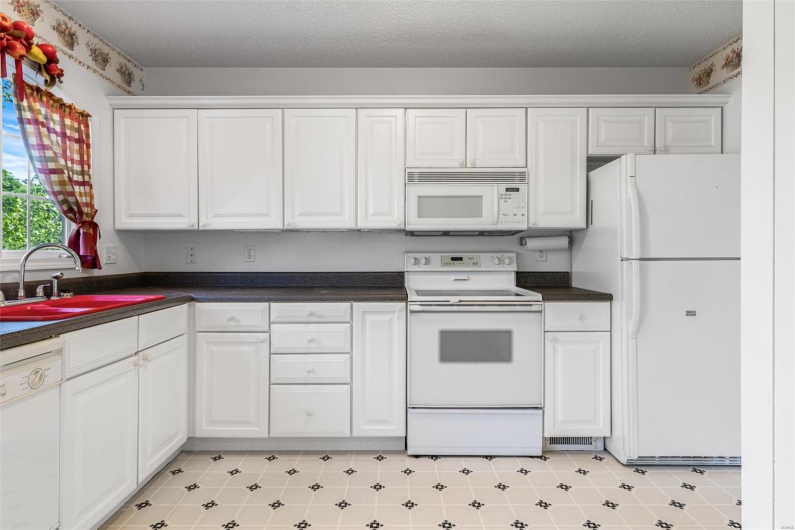 Kitchen with white appliances, dark countertops, a sink, and white cabinets