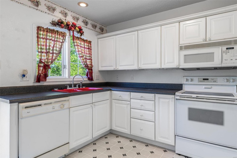 Kitchen with white appliances, white cabinets, dark countertops, and a sink
