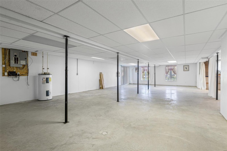 Partially finished Basement with a drop ceiling, electric panel, and electric water heater