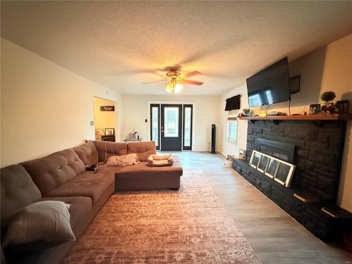 Living room with light wood-type flooring, ceiling fan, a textured ceiling, and a stone fireplace