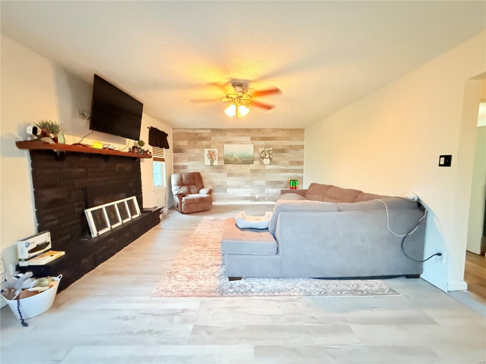 Living room featuring a glass covered fireplace, wood finished floors, and a ceiling fan