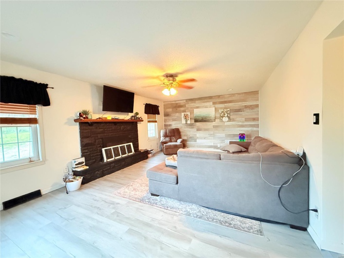 Living room featuring a ceiling fan, a healthy amount of sunlight, a fireplace with raised hearth, and an accent wall