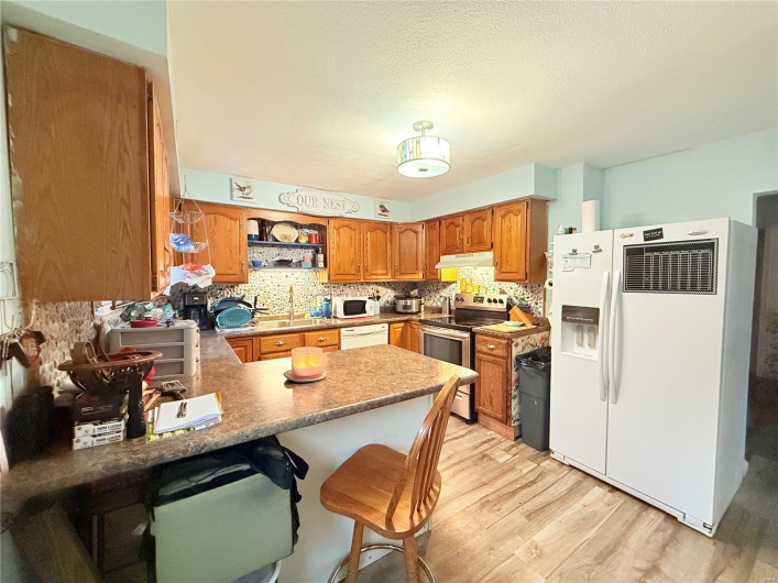 Kitchen with light wood-style floors, under cabinet range hood, white appliances, a peninsula, and backsplash