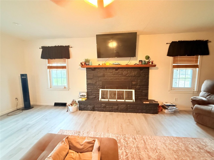 Living room featuring baseboards, wood finished floors, and a stone fireplace