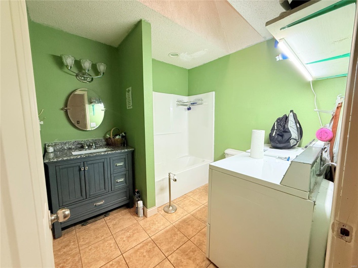 Laundry area with laundry area, washer and dryer, a sink, a textured ceiling, and light tile patterned flooring