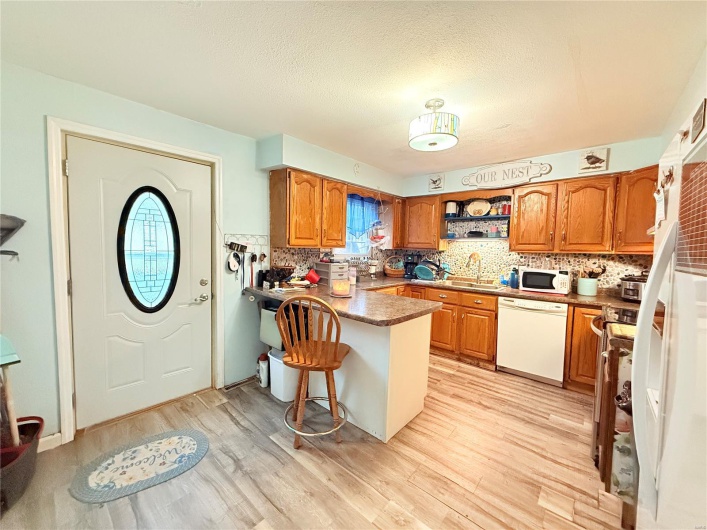 Kitchen with a sink, a peninsula, brown cabinetry, and white appliances