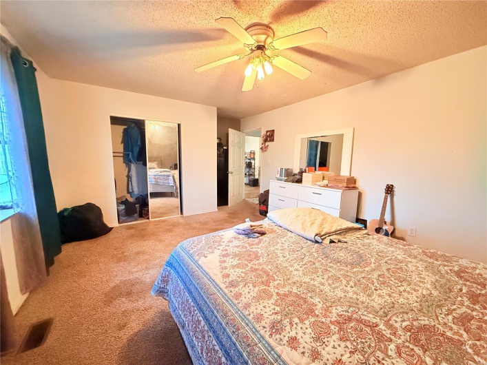 Bedroom with a closet, light carpet, visible vents, a ceiling fan, and a textured ceiling