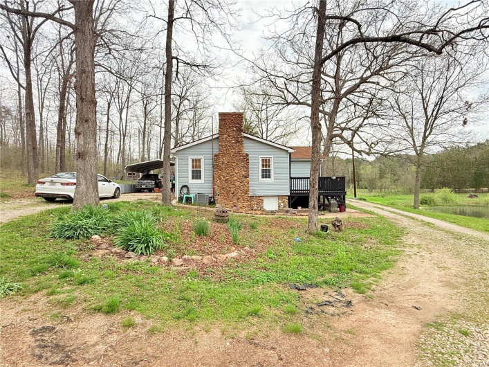 View of side of property featuring a chimney, dirt driveway, a wooden deck, and a carport