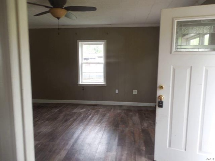 Living room with baseboards, ornamental molding, a ceiling fan, and dark wood-type flooring