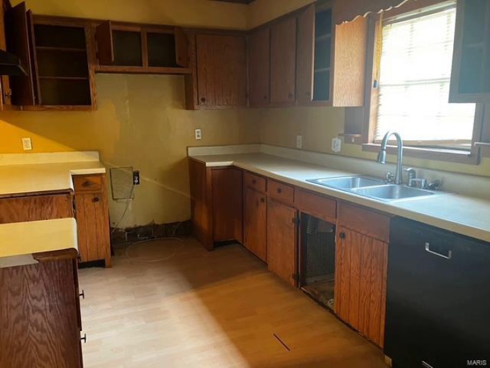 Kitchen with a sink, light wood finished floors, light countertops, black dishwasher, and glass insert cabinets