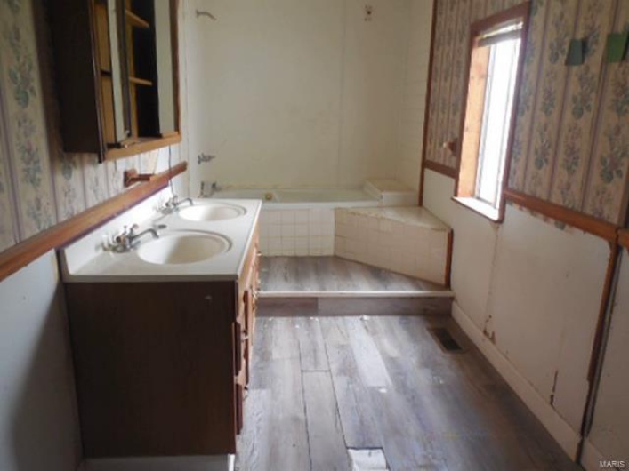Full bathroom featuring a sink, tiled bath, wallpapered walls, and wood finished floors