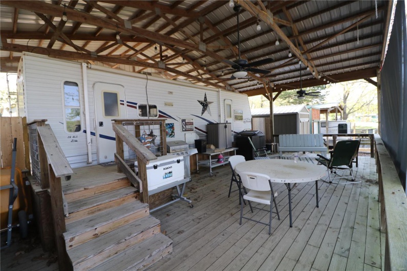 Wooden terrace featuring a storage unit, a ceiling fan, an outbuilding, and outdoor dining space