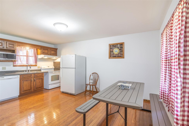 Kitchen featuring white appliances, a sink, under cabinet range hood, light wood-style floors, and brown cabinets