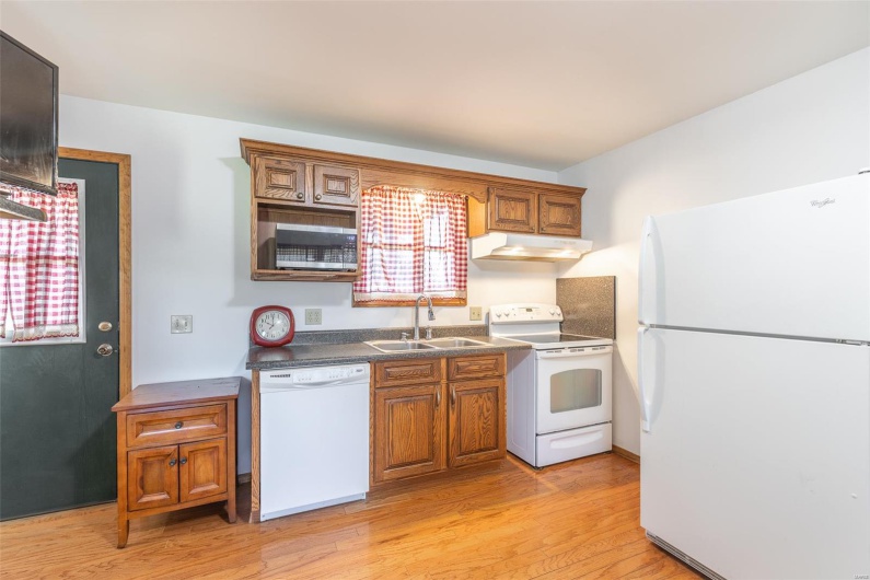 Kitchen featuring white appliances, a sink, under cabinet range hood, light wood-style flooring, and brown cabinets