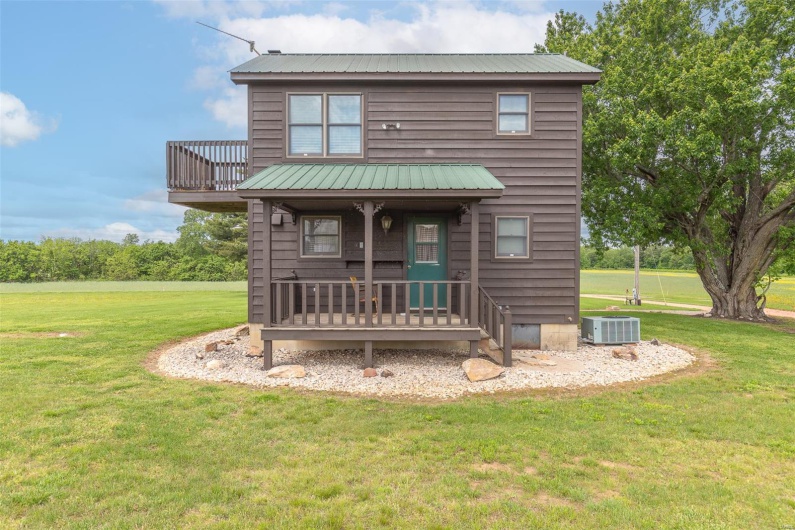 View of front of home with central air condition unit, metal roof, a front yard, and a porch