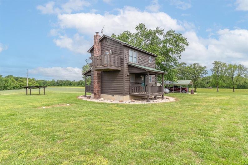 Back of house with a chimney, a lawn, and a balcony