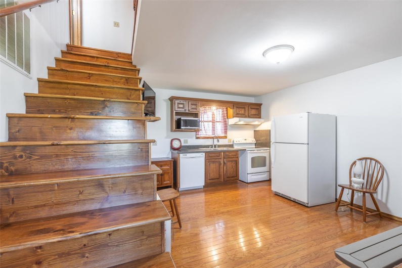 Kitchen featuring white appliances, a sink, under cabinet range hood, light wood finished floors, and brown cabinetry
