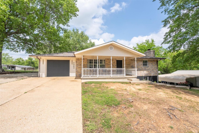 Ranch-style home with a porch, driveway, a chimney, brick siding, and an attached garage