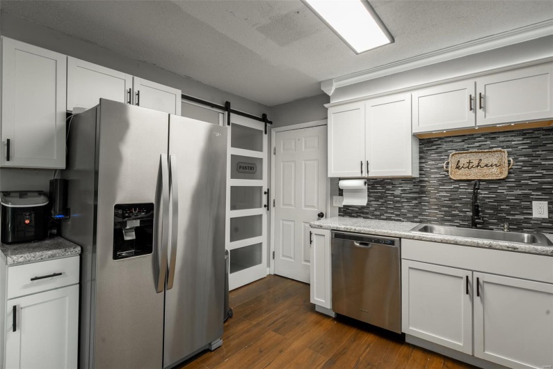 Kitchen featuring a barn door, white cabinets, dark wood finished floors, backsplash, and stainless steel appliances