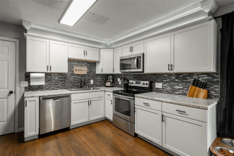 Kitchen with a sink, appliances with stainless steel finishes, dark wood-style flooring, and light countertops