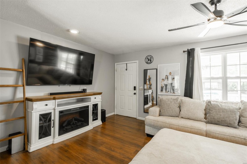 Living area featuring a fireplace, a ceiling fan, a textured ceiling, and dark wood-type flooring