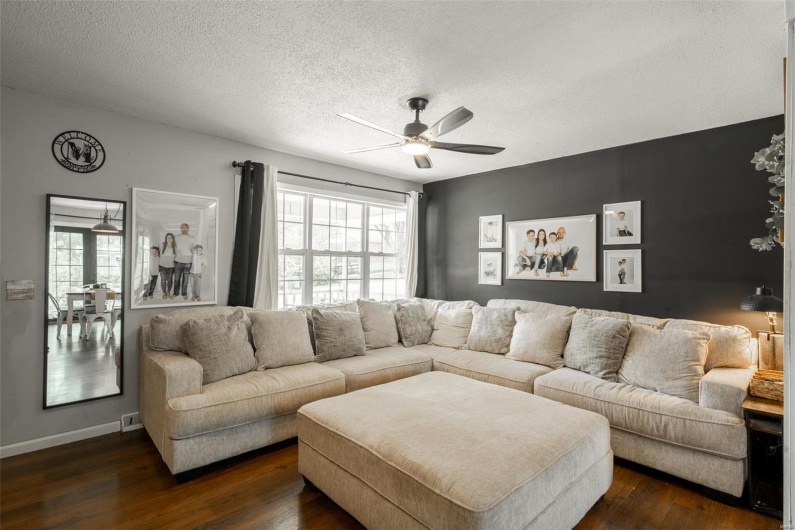 Living room with a textured ceiling, ceiling fan, plenty of natural light, and dark wood-type flooring