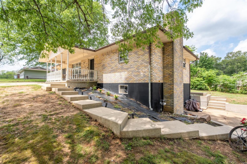 View of side of home featuring a chimney, a porch, and brick siding