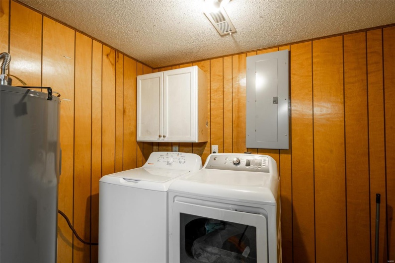 Clothes washing area featuring visible vents, electric panel, electric water heater, separate washer and dryer, and cabinet space