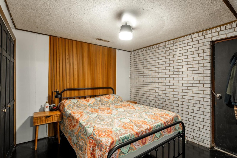 Bedroom featuring a ceiling fan, a textured ceiling, brick wall, visible vents, and a closet