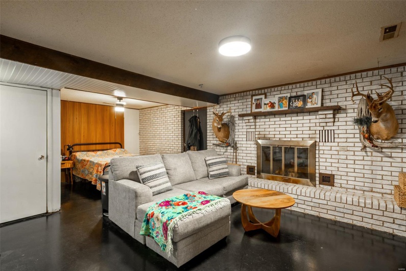 Living area featuring a textured ceiling, brick wall, finished concrete flooring, visible vents, and a fireplace
