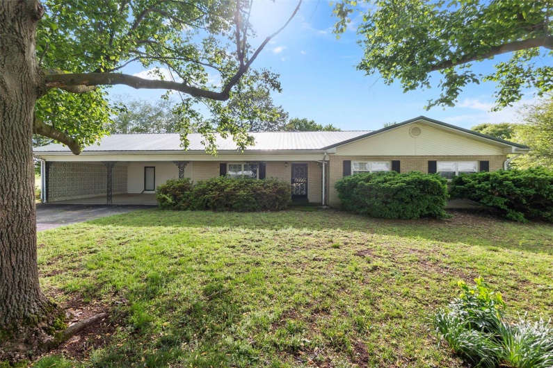 Single story home featuring driveway, metal roof, a front yard, a carport, and brick siding