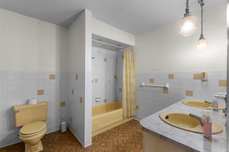 Bathroom featuring a sink, toilet, shower / bath combo with shower curtain, a wainscoted wall, and tile walls