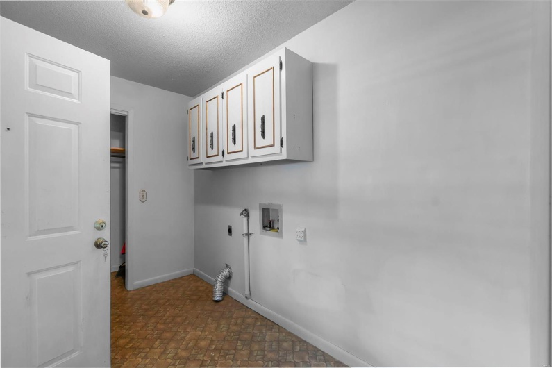 Laundry room with stone finish floor, washer hookup, a textured ceiling, cabinet space, and baseboards