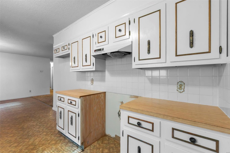 Kitchen with a textured ceiling, butcher block countertops, white cabinetry, decorative backsplash, and under cabinet range hood