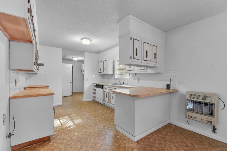 Kitchen with backsplash, dishwasher, baseboards, a peninsula, and heating unit