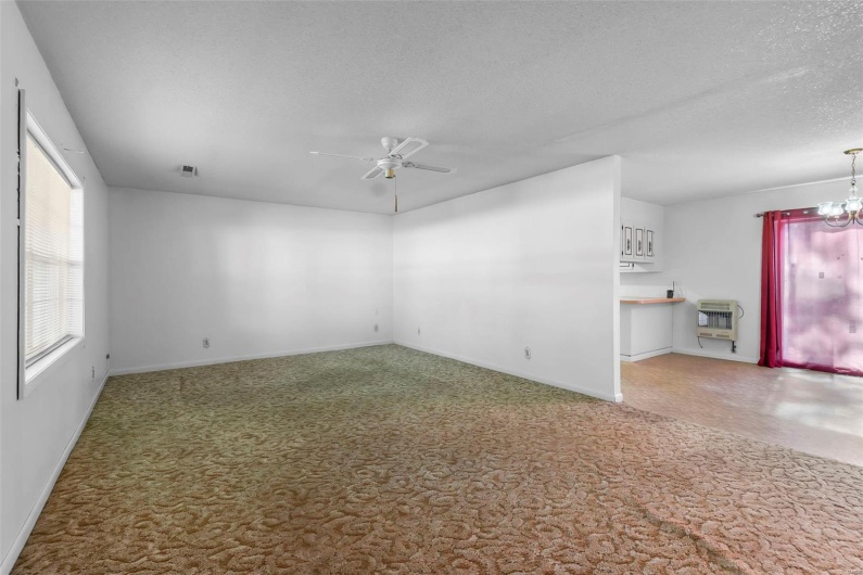 Carpeted empty room featuring a textured ceiling, heating unit, baseboards, and ceiling fan with notable chandelier